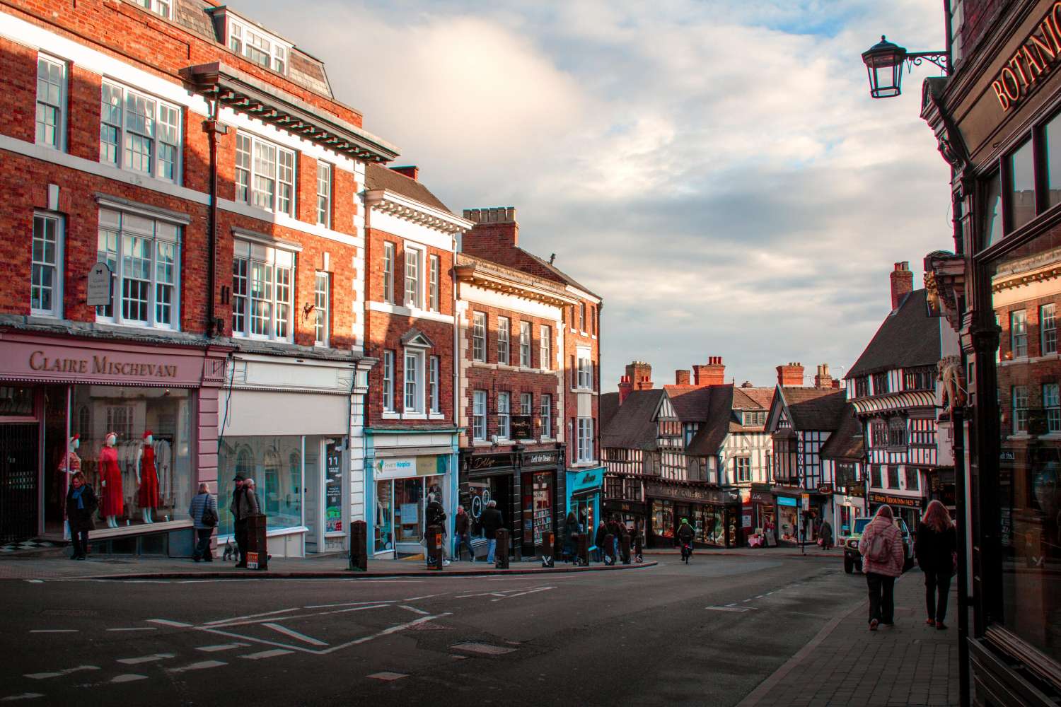 A UK high street with the sun shining over the buildings and hitting the shop fronts