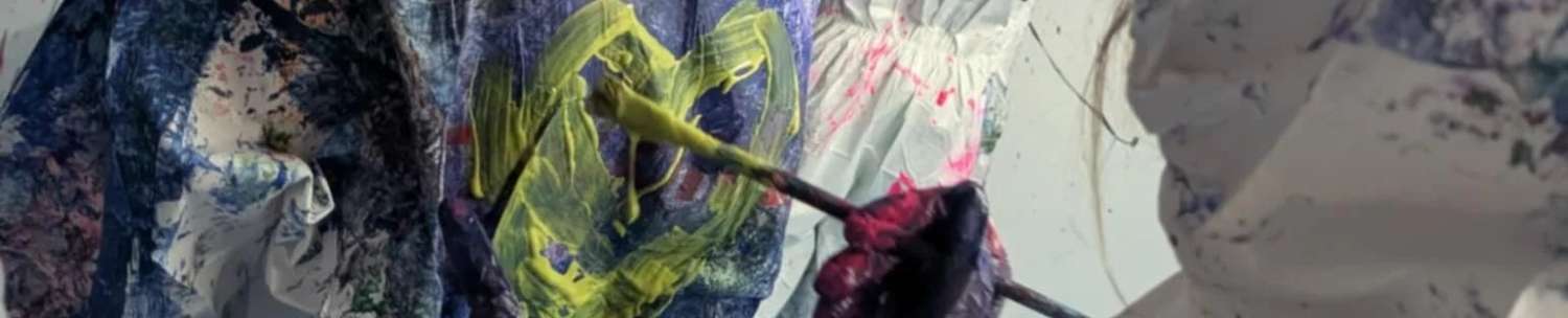 3 people wearing white protective clothing taking part in SplatLab with paint all over the walls and the 3 people, with one of them painting a yellow heart on the back of another