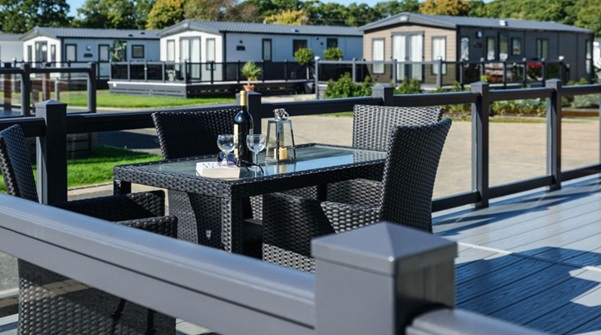 A bottle of wine and glasses sitting on a table on some decking at a holiday park