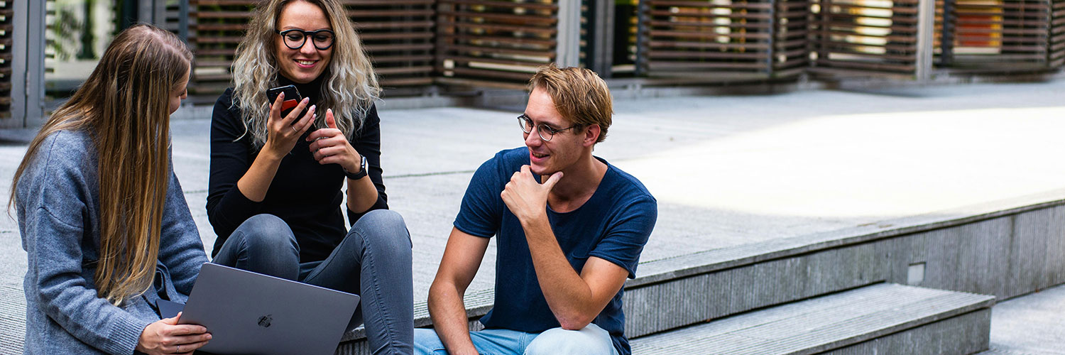 three people talking with one of their phone and another on their laptop
